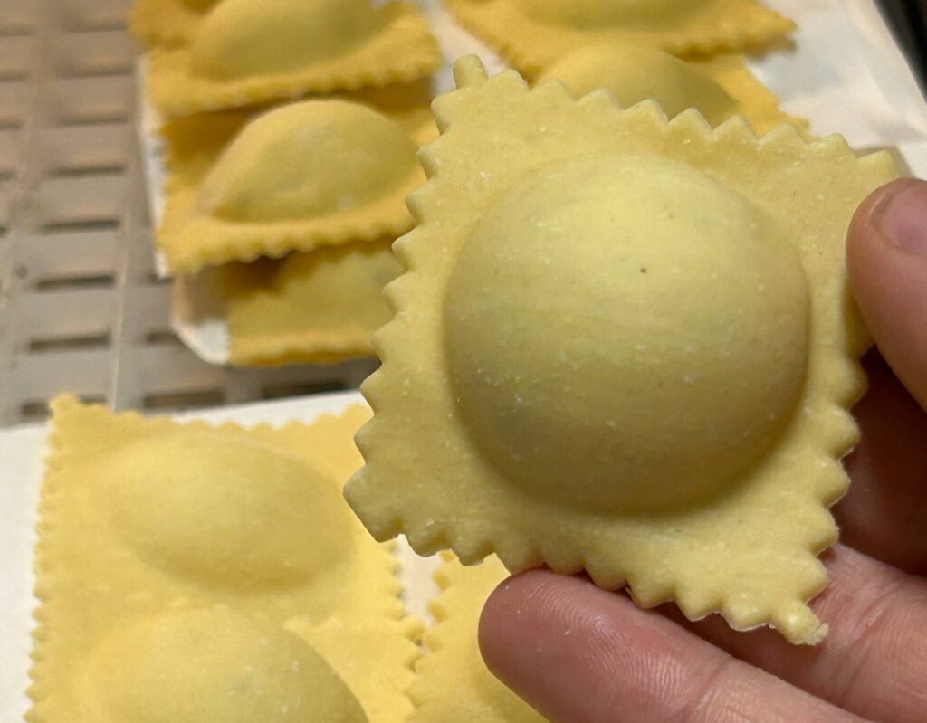 Raviolo di pasta fresca all'uovo con il bordo dentellato, tenuto in mano