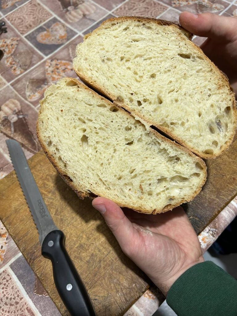 Pane di semola tagliato a metà, con la mollica gialla e alveolata, tenuto in mano sopra un tagliere
