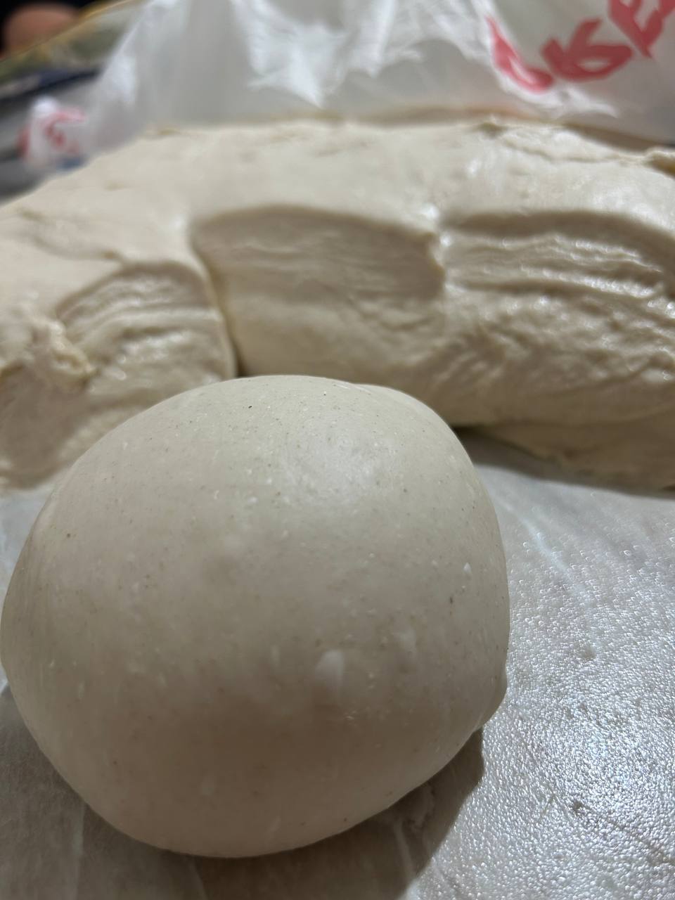 Palla di impasto liscia sul banco, accanto a un impasto ripiegato in lievitazione
