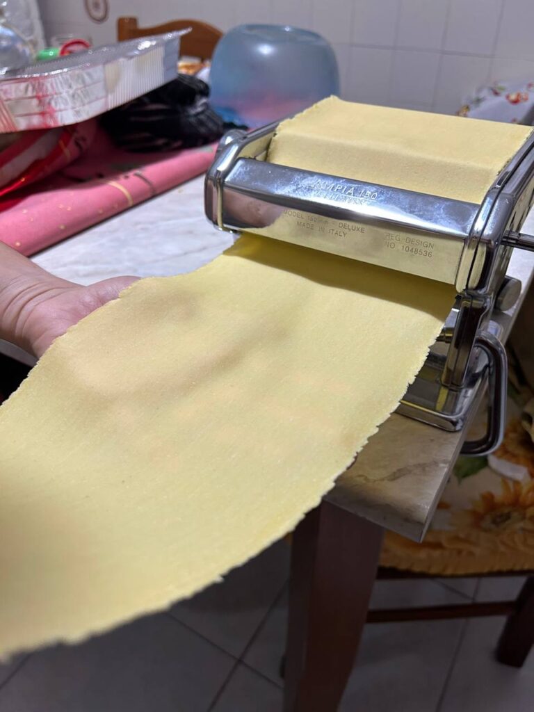 Sfoglia all'uovo sottile e liscia che esce dalla macchina per la pasta, sorretta da una mano