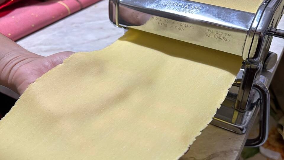 Sfoglia all'uovo sottile e liscia che esce dalla macchina per la pasta, sorretta da una mano