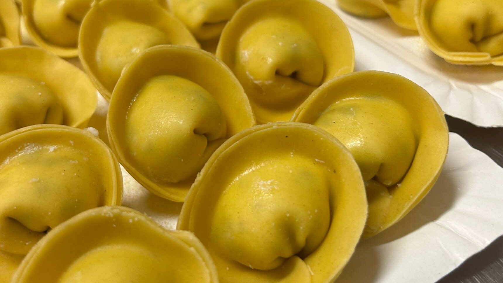 Tortelli tondi di pasta all'uovo con la chiusura ad anello, appoggiati su un foglio di carta